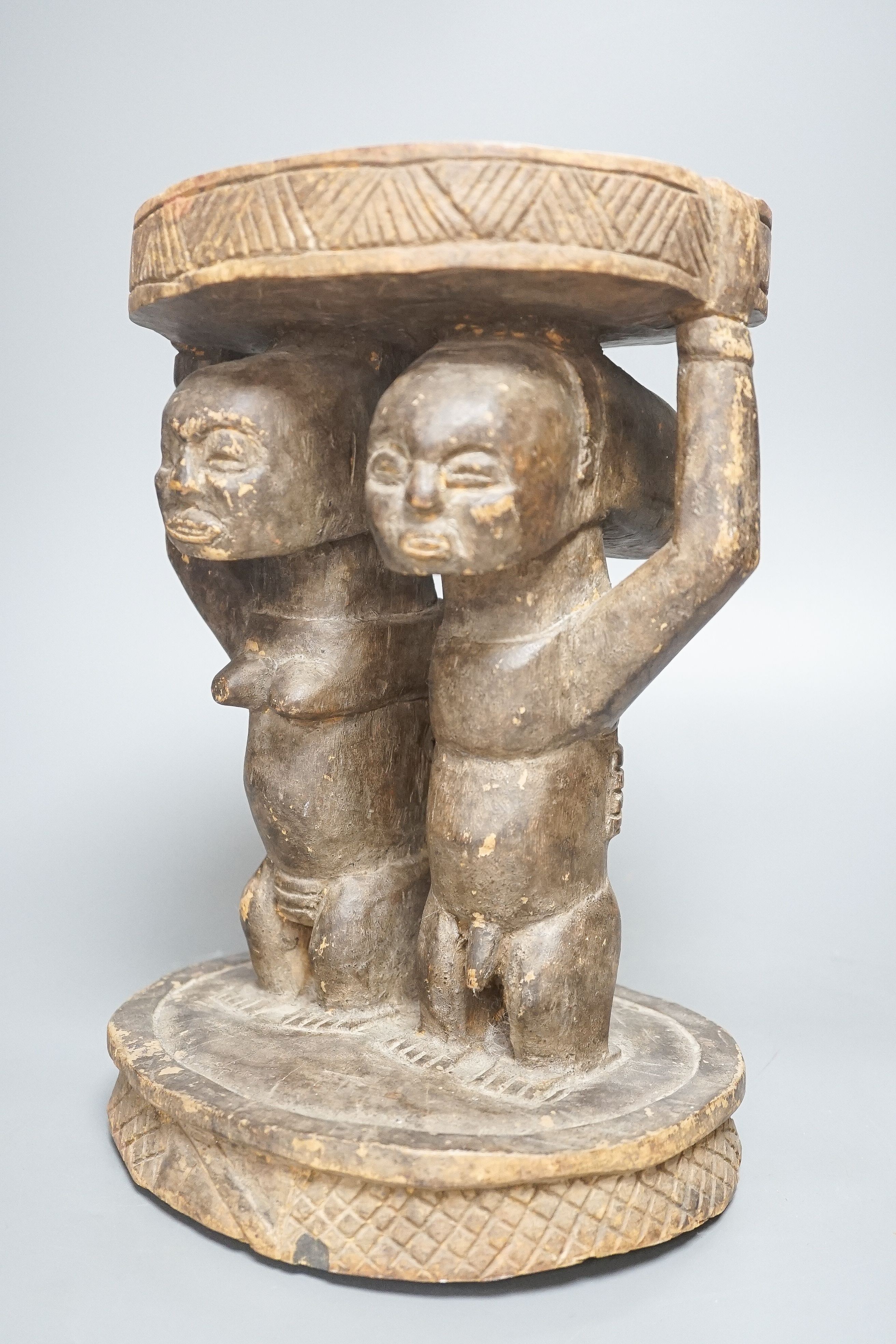 A Yoruba carved wood stool, modelled with male and female figures 27cm